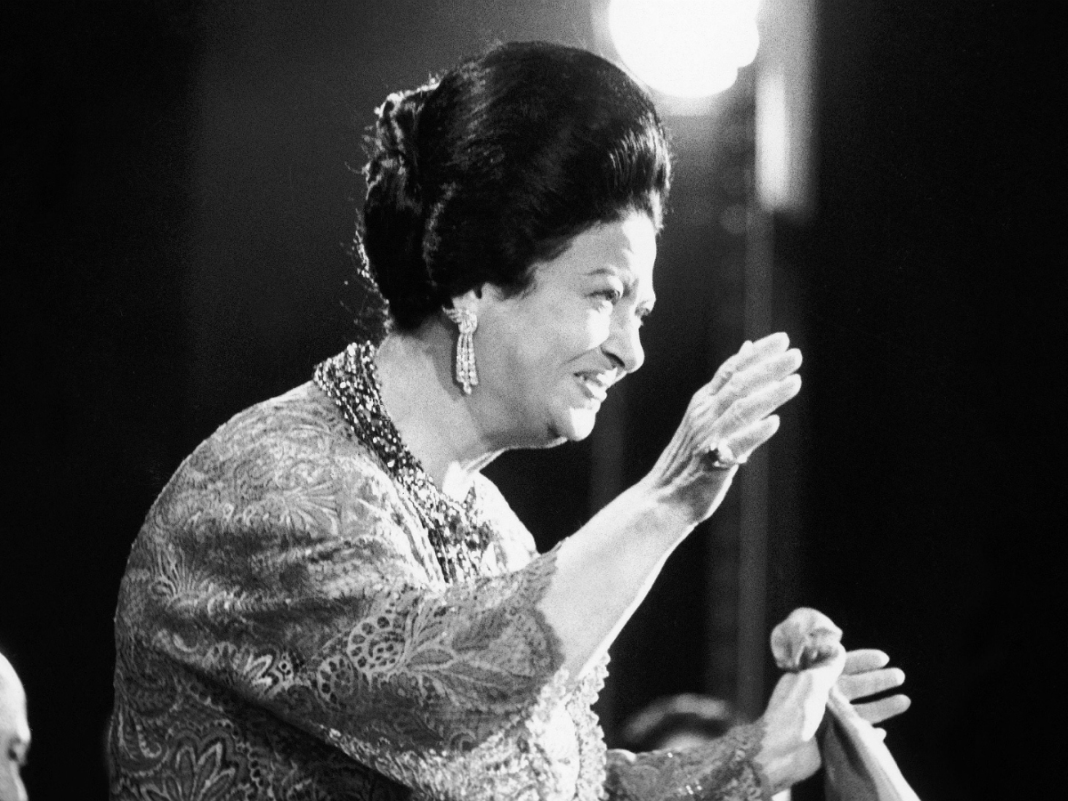 A black and white photo of Umm Kulthum performing in her later years, holding her signature silk handkerchief, known in Arabic as “mandeel”