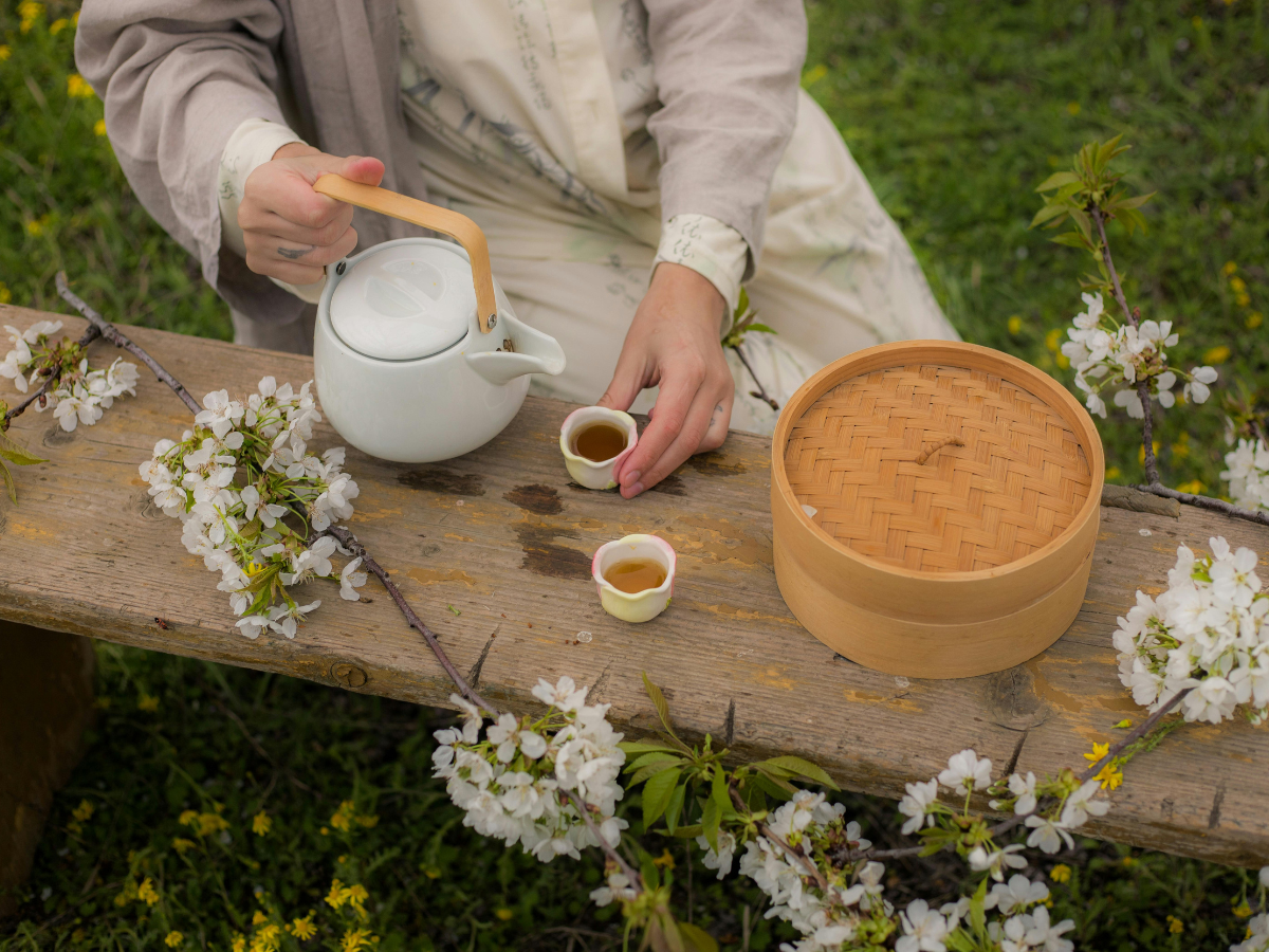 Image alt text: Herbal tea being poured into miniature tea bowls, surrounded by cherry blossom flowers (sakura)