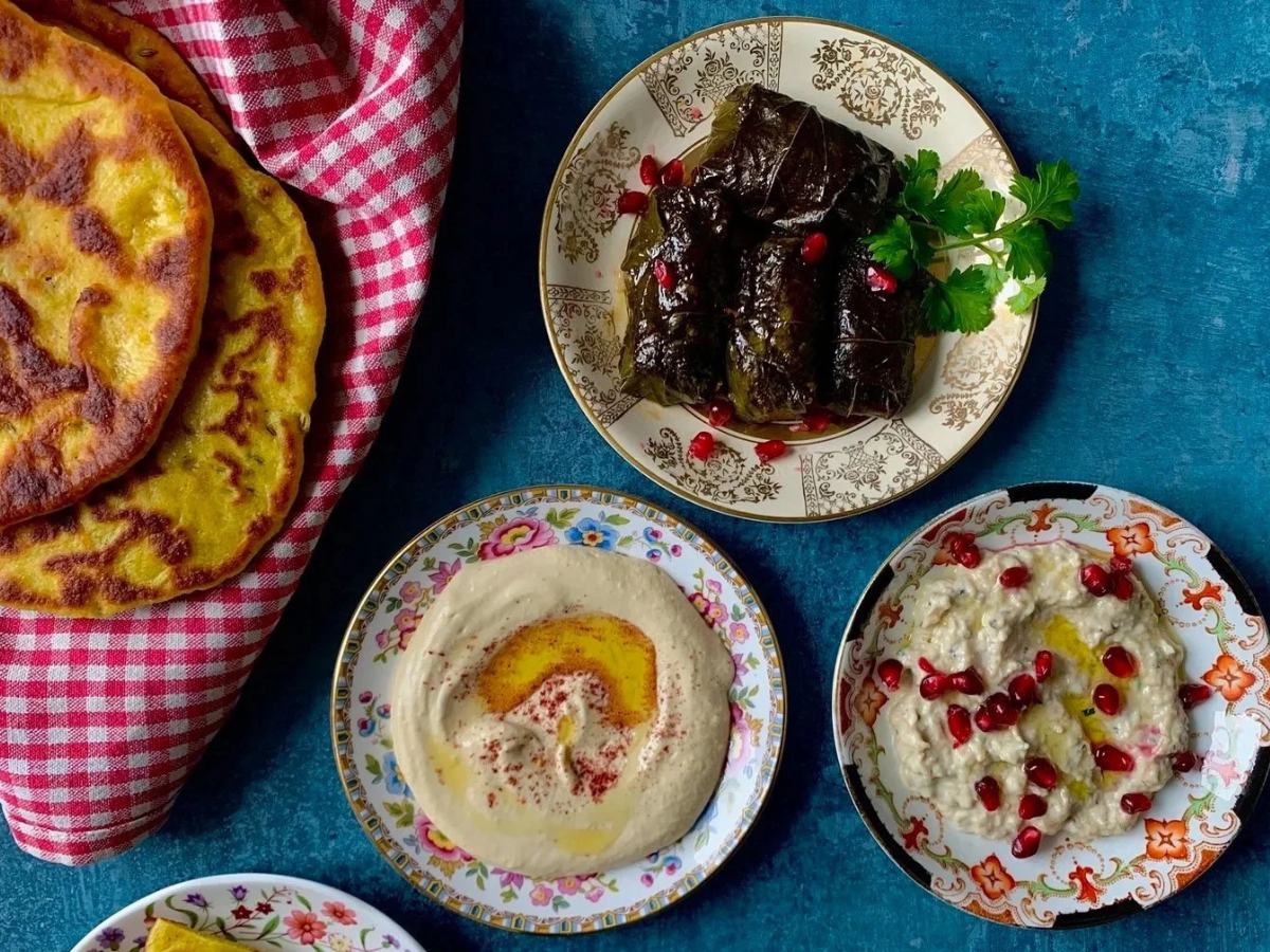 A small Palestinian mezze / mezza spread consisting of taboon bread, hummus, mutabbal / moutabbal, and warak enab / stuffed vine leaves